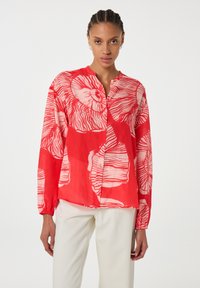 Rote Bluse mit langen Ärmeln, Knopfverschluss vorne und lockerer Passform. Sie hat kontrastierende weiße Blumenmuster und eine weiche Textur.