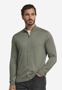 Ljusgrön zip-up jacka gjord av stickat material. Har h ög krage och långa ärmar, med ribbade muddar och rak nederkant.