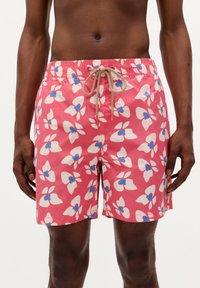 Pink swim shorts featuring a floral pattern in white with blue accents. Elastic waistband with a drawstring. Lightweight fabric.