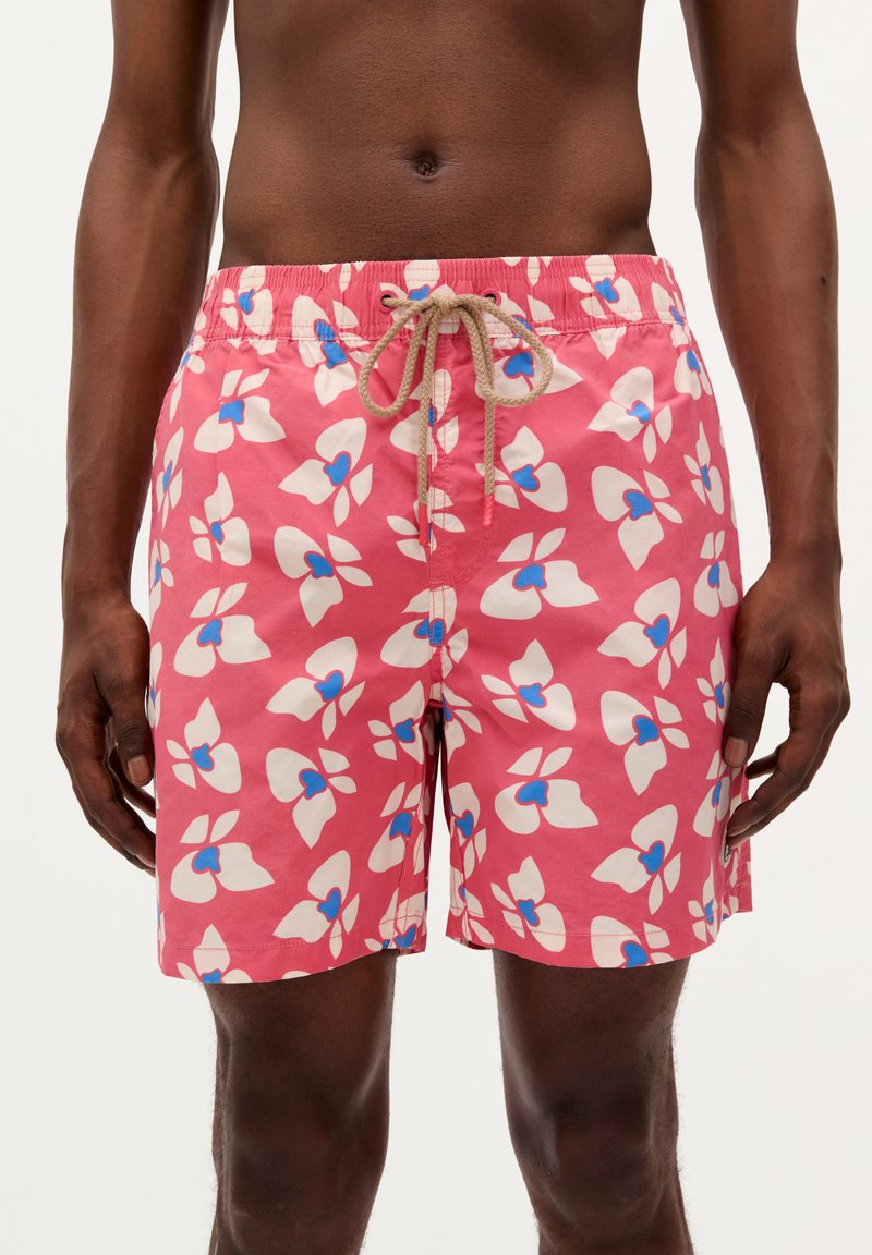 Pink swim shorts featuring a floral pattern in white with blue accents. Elastic waistband with a drawstring. Lightweight fabric.