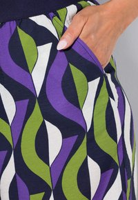 Tessuto con motivo caratterizzato da forme swirling in viola, verde e bianco su uno sfondo scuro; include una tasca laterale. Texture liscia.