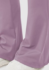 Close-up van lavendelkleurige broek die witte gestructureerde sneakers bedekt, met details van de stof en stiksels aan de zoom.