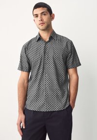 Camicia a maniche corte con motivo geometrico bianco e nero, realizzata in tessuto leggero, con chiusura frontale a bottoni e colletto.