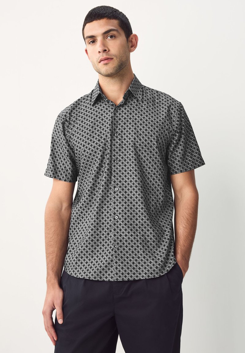Camicia a maniche corte con motivo geometrico bianco e nero, realizzata in tessuto leggero, con chiusura frontale a bottoni e colletto.