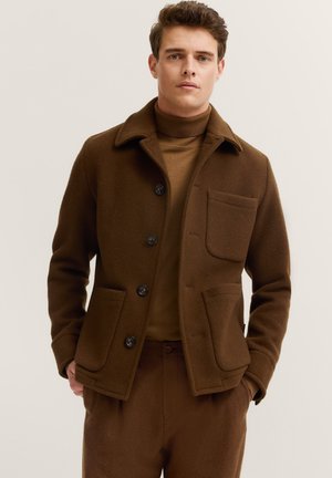 Braune Wollmischung Jacke mit Kragen, zwei vorderen Taschen und schwarzen Knöpfen; kombiniert mit einem passenden braunen Rollkragenpullover. Softes Material.