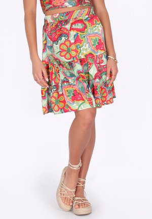 Vrouw die een kleurrijke, met bloemen bedrukt knielang rokje draagt en beige veterespadrilles, staand met gekruiste benen.