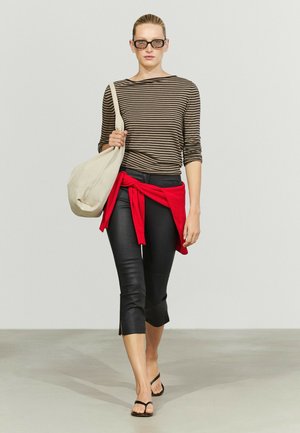 Femme marchant, portant un pantalon noir court, un haut rayé à manches longues, un pull rouge noué à la taille, des sandales noires, un grand sac beige et des lunettes de soleil.