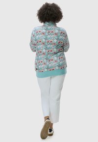 Giacca a fantasia floreale di colore azzurro chiaro, con maniche lunghe, colletto e cintura a contrasto. Abbinata a pantaloni bianchi e scarpe casual.