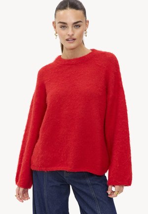 Rode, fluffy trui met een ronde hals en lange mouwen. Heeft een relaxed fit en een zachte textuur, gecombineerd met donkerblauwe jeans.