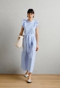 Hellblau-weiß gestreiftes Kleid mit Rüschensäumen, tailliertem Bund und gestuftem Rock. Kombiniert mit einer cremefarbenen Handtasche und flachen Schuhen.