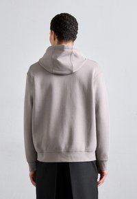 Lys grå hettegenser med en myk tekstur, løs passform og ribbede mansjetter, sammen med mørke bukser. Enkel, moderne design uten pynt.