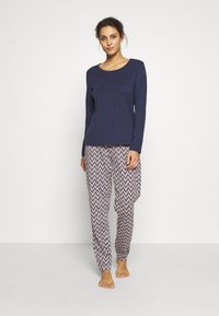 Haut à manches longues bleu marine avec une petite poche poitrine, associé à un pantalon de pyjama rose pâle à motifs avec des lignes en zigzag. Matière en coton douce.