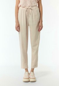 Pantaloni beige, leggeri e dal taglio comodo, con vita elasticizzata e cordoncino regolabile. In abbinamento a delle scarpe da ginnastica eleganti e casual.