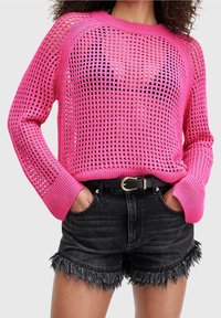 Różowy sweter z dzianiny o luźnym, otwartym splocie oraz ściągaczami na mankietach, w zestawieniu z czarnymi szortami dżinsowymi z postrzępionymi krawędziami i czarnym paskiem.