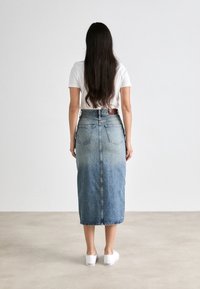 Jeansmaxiklänning med en gradvis ljus till mörkblå gradient, två bakfickor och ett bälte i midjan, kombinerad med en enkel vit t-shirt.