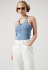 Top de tirantes de mezclilla con acabado azul desgastado, con diseño de espalda nadadora y sutil fruncido lateral; combinado con pantalones blancos de tiro alto.
