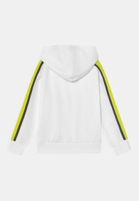 Felpa bianca con cappuccio regolabile, maniche lunghe con strisce laterali giallo neon e nere, e un tessuto texturizzato.