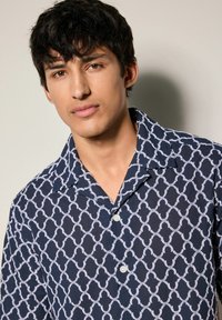 Cămașă scurtă de navy cu un model geometric alb, având un guler clasic și închidere cu nasturi, fabricată dintr-un material ușor.