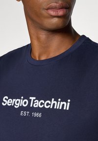 Marineblå bomuld t-shirt med rund hals og hvid trykt tekst "Sergio Tacchini EST. 1966" på forsiden.