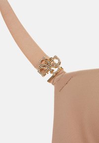 Naakte bh-band met een gouden haak die een ingewikkeld ontwerp en kleine rhinestones bevat. Gladde textuur met een matte afwerking.