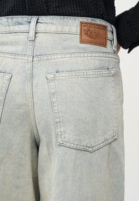 Τζιν με ανοιχτόχρωμο ξεβάμμα, πίσω όψη με ορατές πίσω τσέπες και καφέ δερμάτινο ταμπέλα της μάρκας Element στη μέση.