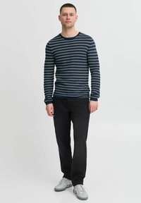 Camicia a righe blu navy e crema a manica lunga, aderente, abbinata a jeans neri e sneakers bianche. Tessuto liscio, design casual.