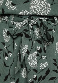 Tecido verde com uma superfície texturizada, apresentando um padrão floral em branco e preto. Inclui um detalhe de cinto combinando.