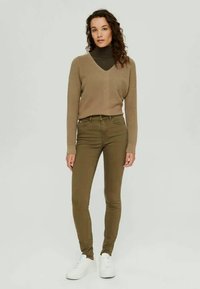 Beige ribbed sweater with a V-neck, paired with olive green skinny jeans and white sneakers. The outfit has a fitted silhouette.