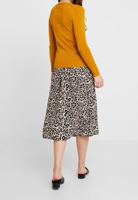 Senapsgul långärmad ribbad tröja i kombination med en knä-lång krämfärgad kjol med svart leopardmönster. Svarta slip-on skor fulländar looken.