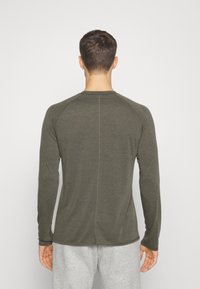 Dunkelgrünes Langarmshirt mit glatter Textur und Raglanärmeln, mit einer mittigen Naht auf der Rückseite und dezenten Stickdetails.