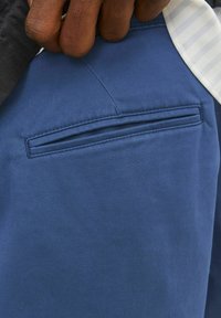 Pantalons bleu foncé avec une poche arrière plate ornée de coutures discrètes, fabriqués en tissu lisse et texturé.