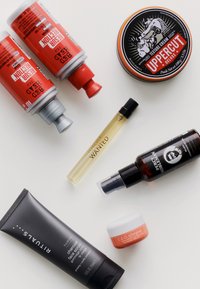 Różnorodne produkty do pielęgnacji na jasnym tle: dwie czerwono-szare tuby, czarny słoik, mały pomarańczowy słoik i przezroczyste butelki z rozpylaczem.
