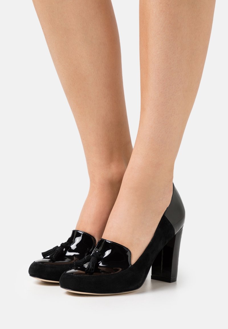 Chaussures à talons hauts noires combinant cuir verni et daim, avec un bout arrondi, des accents à pampilles, et un talon épais.