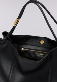 Svart läderhandväska med slät textur, utrustad med detaljer i guldmetall, ett innerfack med dragkedja och en mjuk, slapp design.