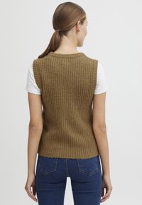 Brun ribbestrikket vest med rund hals, ermeløs design og en litt kortere passform, lagd over en hvit t-skjorte.