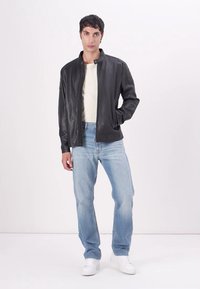Chaqueta de cuero negra con cremallera y un alto cuello, diseño ajustado y puños acanalados, combinada con jeans de color azul claro y zapatillas blancas.