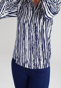 Camicetta a righe blu navy e bianche realizzata in tessuto leggero, con colletto e maniche lunghe con polsini abbottonati.