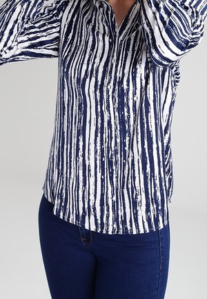 Chemise rayée bleu marine et blanche en tissu léger, avec un col et des manches longues avec des poignets à boutons.