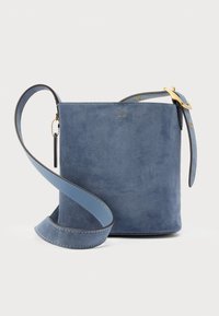 Niebieska zamszowa torebka typu crossbody marki Coach z regulowanym paskiem i złotą klamrą na białym tle.