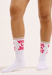 Chaussettes blanches de crew avec un texte "Viva La Juicy" rose, un revers rayé vert et rouge, une texture côtelée et un design de longueur mi-mollet.