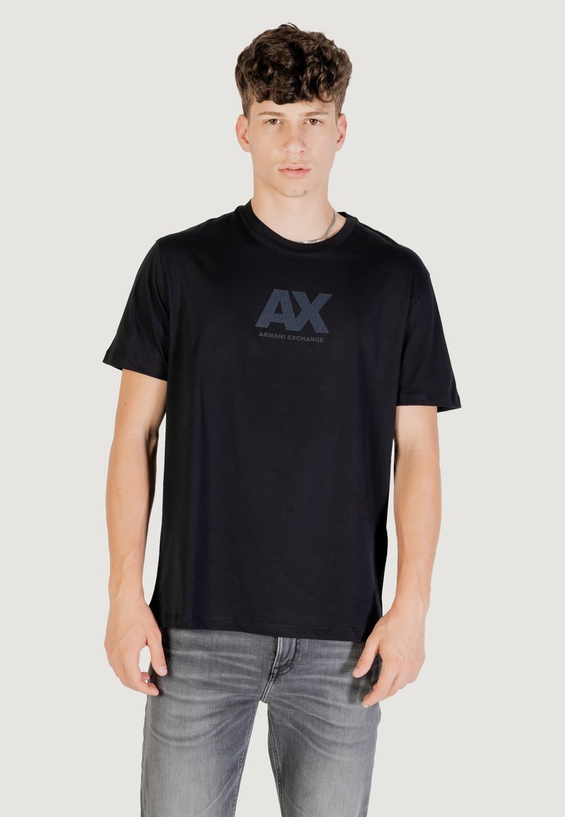 T-shirt en coton noir avec un logo AX ton sur ton sur la poitrine, des manches courtes et un col rond, associé à un jean gris.