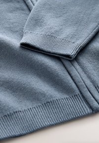 Blå strikket sweater med tekstureret finish, ribstrikkede manchetter og kant, med lynlåslukning og glat stof.