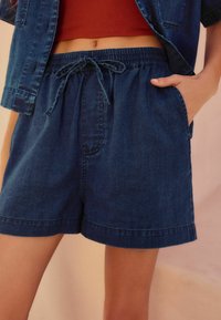 Jeansshorts med elastisk midja och dragsko, med sidofickor och avslappnad passform. Mörkblå färg med en mjuk textur.