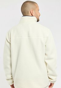 Weiße Fleecejacke mit hohem Kragen und strukturiertem Finish, entspanntem Schnitt und Rückennaht-Detail.