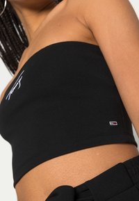 Top negro sin tirantes hecho de tela suave, con logo bordado en blanco y una pequeña etiqueta con la marca en el dobladillo.