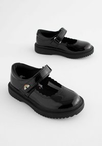 Chaussures noires en cuir verni de style Mary Jane, avec une sangle à boucle auto-agrippante et des bords festonnés, reposant sur une semelle en caoutchouc.