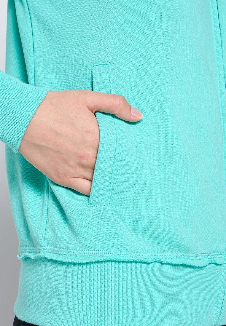 Pullover in felpa verde menta con tasca frontale e orlo testurizzato. Il materiale sembra morbido e leggermente elastico. Design semplice senza motivi.