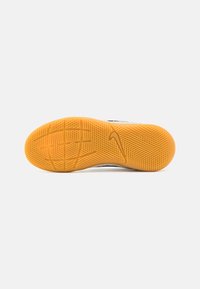 Suela de goma naranja de una zapatilla con un patrón de agarre texturizado y el logo del swoosh de Nike visibles sobre un fondo blanco.