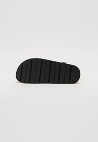 Talpa de sandală din cauciuc negru cu caneluri orizontale pentru aderență, formă rotundă și textură netedă. Design minimalist, fără logo-uri vizibile.