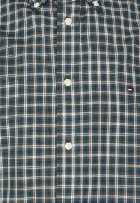 Camisa de botones en un patrón de cuadros en navy, verde y blanco; presenta botones blancos y un pequeño logo en el lado izquierdo. Material de algodón, tejido texturizado.